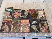 Image of lot showing all 10 pulp fiction paperbacks laid flat on a beige towel with colorful vintage illustrated covers.