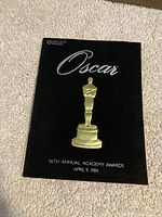 Front cover of the 1984 Oscar program booklet with a black background, silver 'Oscar' text, and a gold statuette illustration. Date and event details displayed at the bottom.