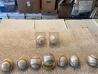 Wide shot of all nine baseballs in the lot, showing seven autographed baseballs laid out in front with two unsigned baseballs in plastic cases behind them.