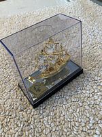 Full view of gold plated boat figurine inside clear protective display case on a textured carpet.
