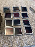 Photograph of 12 metal-framed slides laid out on carpet. Slides are black or darkened, with the metal frames visible.