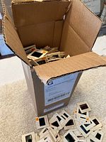 Image of open cardboard box filled with 35mm photographic slides loosely stacked inside, showing mounts with Kodak branding and handwritten annotations.