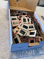 Cardboard box filled with hundreds of loose photo slides with paper frames inside.