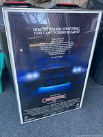 Front of framed John Carpenter's Christine movie poster showing fold lines and text with headlights graphic.