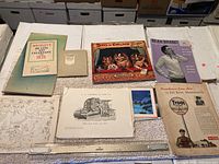 Top view of assorted vintage ephemera including Wrigley's 1935 calendar, Bear Brand booklet, cartoon calendars, technical drawings, and advertisements.