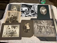Photo of a group of old photographs on a textured white cloth, featuring various portraits and group shots, some mounted on dark mats.