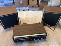 Lloyd's 8-track player and two matching speakers shown on a textured surface with boxes in the background.