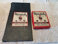 Monopoly game box and black storage pouch with matching label showing Popular Edition by Parker Brothers.