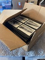 Open cardboard box filled with photographic album pages showing mounted black and white photos, about a hundred sheets visible.