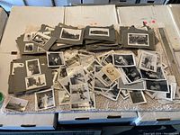 Wide shot of hundreds of old photos, some mounted on gray album pages, spread out on a white surface next to a ruler.