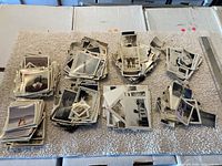 Overview of multiple stacks of old photographs, black & white and color, some curling and varying sizes, arranged on a cloth surface.