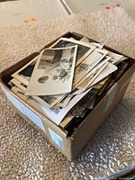 Cardboard box filled with vintage black and white photographs stacked and overflowing.