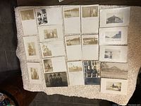 Photo showing the front side of 19 vintage postcards arranged on a surface, displaying sepia photographs of people, buildings, and outdoor scenes. Few cards have visible handwriting and staining.