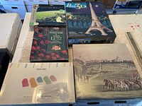 Five puzzles and games shown on table, including 3D Eiffel Tower puzzle, Planet Earth puzzle, Double Cross John Lutz puzzle, Dominoes game, and vintage horse racing print item.