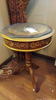 Full view of round accent table showing wood carved base and floral motif on side drawer.