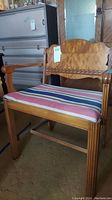 Front view of antique wooden vanity chair featuring striped cloth seat and carved details on wood frame.