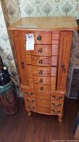 Front view of wooden jewelry armoire showing six drawers, side doors, and dual bottom drawers.