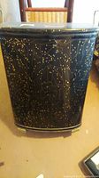 Front view of the vintage MCM style laundry hamper, black with gold dotted pattern.