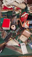 Photo showing a collection of office supplies on a green desk, including red and white flip notebooks, pens, a small clock in a case, shoehorns, and other accessories.