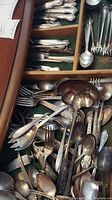 Drawer filled with numerous assorted forks, spoons, knives, and a large scalloped serving spoon with tarnished silver plate finish.