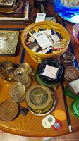 Photo shows a collection of assorted ashtrays, a basket filled with matchbooks, miniature West Point figure, round tokens, and glass coasters on a wooden table.
