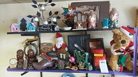 Overview of vintage Christmas decorations and collectibles including bear on bike, Santa figurine, Putz houses, tins, and green NOEL candle holder.