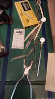 Photo of vintage dental tools including dental picks, mirrors and boxed Capsule Aspirator syringe on green surface.