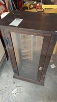 Full view of the vintage wooden display cabinet with glass front door, showing dark wood and visible wear on top surface.