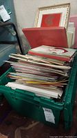 Large green plastic tub filled with piles of assorted vintage greeting cards, some stacked vertically and others horizontally, showing a variety of sizes.