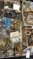 Wide view showing assorted vintage hardware including metal drawer knobs, decorative pulls, brass pieces, light fittings, and small caster wheels.