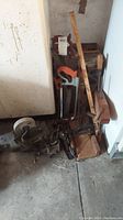 Overall view of assorted vintage tools including grinder, clamps, and saws on concrete floor by wall