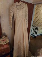 Full view of a long-sleeve vintage wedding gown with detailed lace bodice, floral applique, lace sleeves, and satin skirt with lace hem trim.