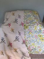 Two floral bedspreads laid out, showing different floral designs side by side. One has vibrant embroidered flowers and the other a detailed floral print.