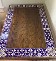 Top view of rectangular table showing the wooden surface and the fully tiled decorative border with blue, yellow, white linens.