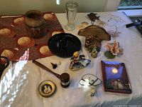 Wide view of all vintage and newer decor items displayed on table including glass vase, ceramic vase, black glass dish, figurines, wall shelf, and various small collectibles.
