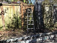 Extension ladder laid flat on gravel with step ladder and T-posts in background