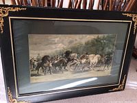 Framed lithograph print showing horses and riders, under glass in an ornate black and gold frame.