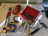 Photo showing entire tool set with aluminum level, red toolbox, orange extension cord, black anti-slip tape, and various hand tools including screwdrivers, pliers, wrench, and hammer.