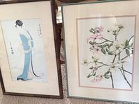 Framed Japanese prints showing Geisha Girl Itsutomi in blue kimono and floral blossoms artwork side by side
