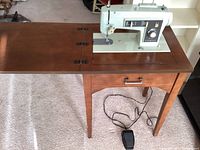 Kenmore model 1302 sewing machine built into wooden sewing table with foot pedal and power cord visible.