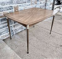 Full view of the table showing woodgrain Formica top and tapered metal legs in need of reattachment.