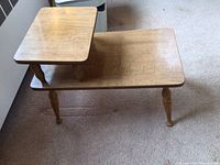Full view of mid-century wood veneer side table on carpet. Shows table top surfaces and turned legs.