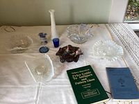 View of entire lot showing milk glass vase, carnival glass bowl, clear dishes with opalescent edges, blue glass, and books