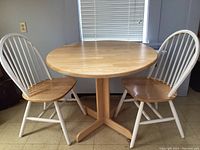 Round maple wood dining table with two white spindle-back chairs, table top round with natural finish