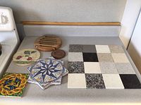 Overall view of the stone coaster tiles, wooden trivets, and ceramic trivets laid out on a counter.