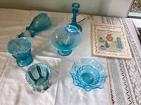 Overview of six vintage blue glass items on white tablecloth including bowls, vase, and candlestick along with a booklet titled 'Opalescent Glass from A to Z'