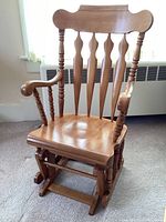 Front view of the vintage wooden glider rocking chair showing contoured wooden seat, carved backrest with vertical spindles, and turned armrests.