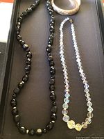 Photo of black beaded necklace, crystal bead necklace, and engraved bangle bracelet on black background.