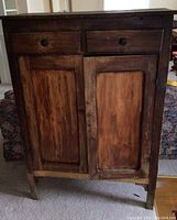 Front view of vintage wooden pie cabinet, showing two drawers with round knobs and double doors with inset panels.