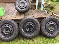 Four black steel rims with mounted snow tires, three Kumho and one Signet, arranged on grass in front of wooden deck.